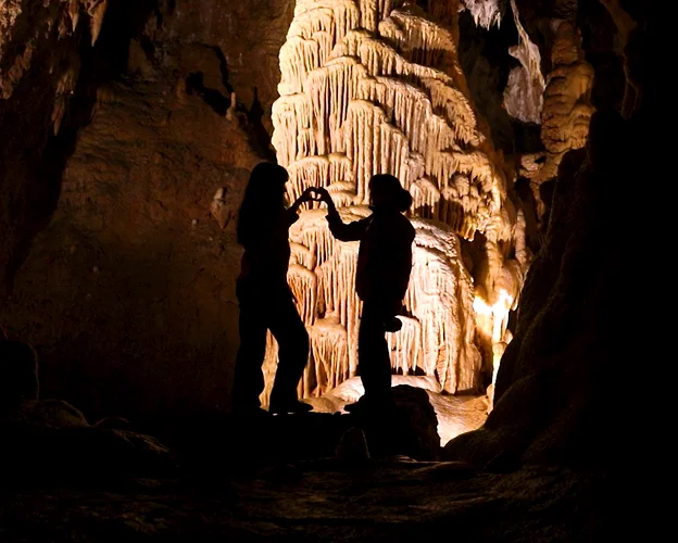 Silhouettes de deux personnes formant un cœur devant une formation rocheuse illuminée dans une grotte à Meyrueis en Lozère 48