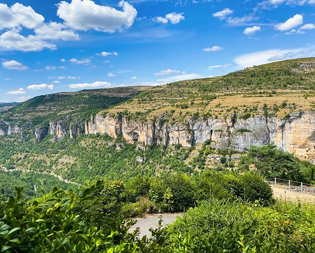 Falaises calcaires spectaculaires surplombant une vallée verdoyante sous un ciel bleu nuageux à Meyrueis en Lozère 48