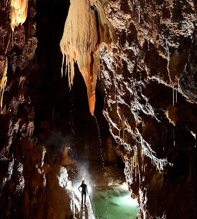 Spéléologue sous une grande stalactite ruisselante, éclairée par une lumière verte sur l'eau à Meyrueis en Lozère 48