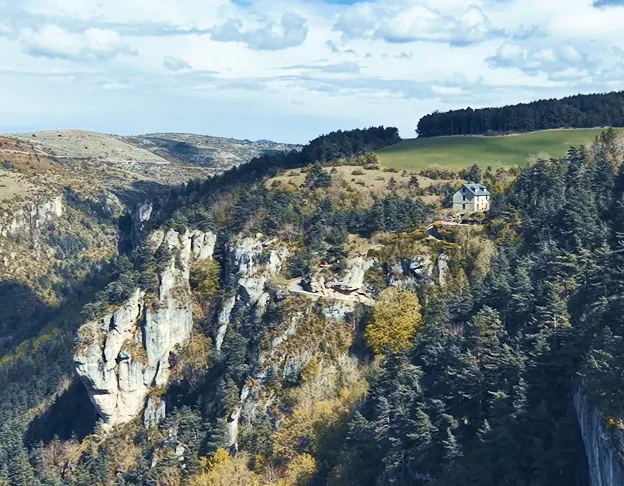Maison isolée sur une falaise verdoyante dominant un canyon montagneux sous un ciel nuageux à Meyrueis en Lozère 48