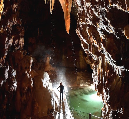 Une personne admire l'intérieur de la grotte de Dargilan : lumière, concrétions, rivière souterraine