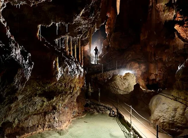 Caverne sombre illuminée avec des stalactites, un bassin et une silhouette humaine à Meyrueis en Lozère 48